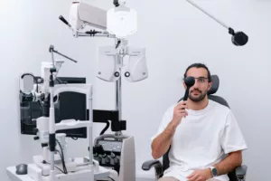 Are Designer Glasses Worth It? Quality, Durability & What You Should Know 1 A male patient undergoing a comprehensive eye exam at an optometry clinic, holding an eye occluder while sitting in an exam chair.