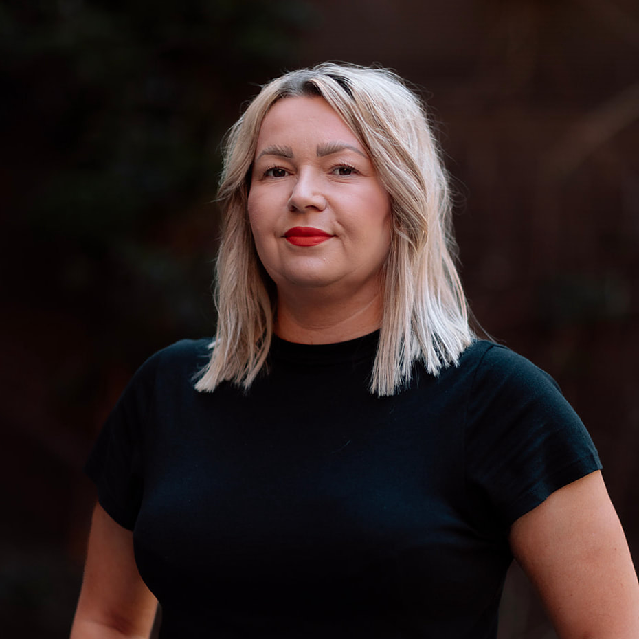 Our Team 15 Headshot of a blonde woman wearing a black t-shirt and red lipstick.