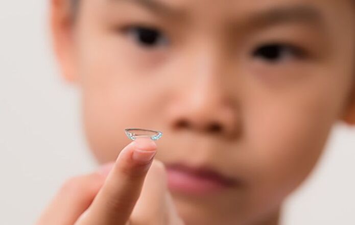 Close-up of a young child holding a soft contact lens on their fingertip, highlighting pediatric contact lens fittings.