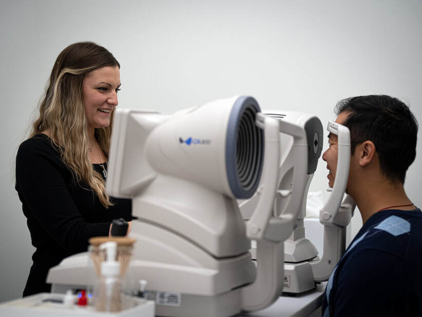 Smiling woman performs eye exam on man using advanced ophthalmic equipment.