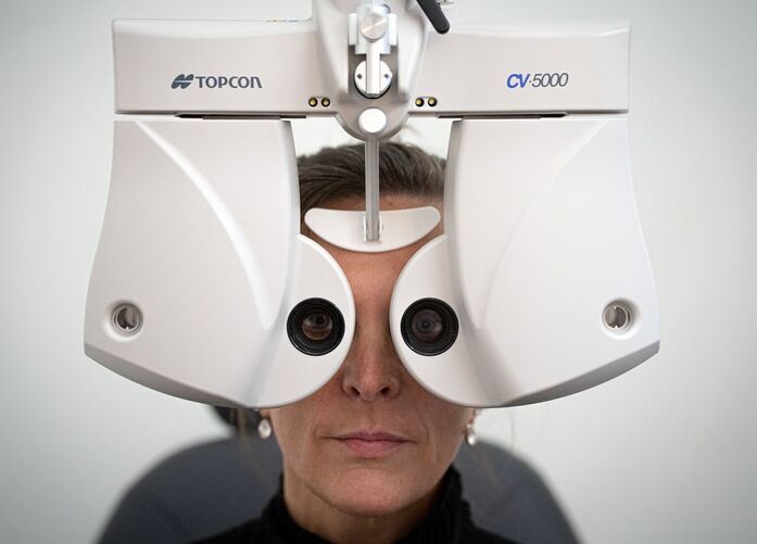Frontal view of a patient looking through a Topcon CV-5000 phoropter during a precision vision exam at an eye clinic.