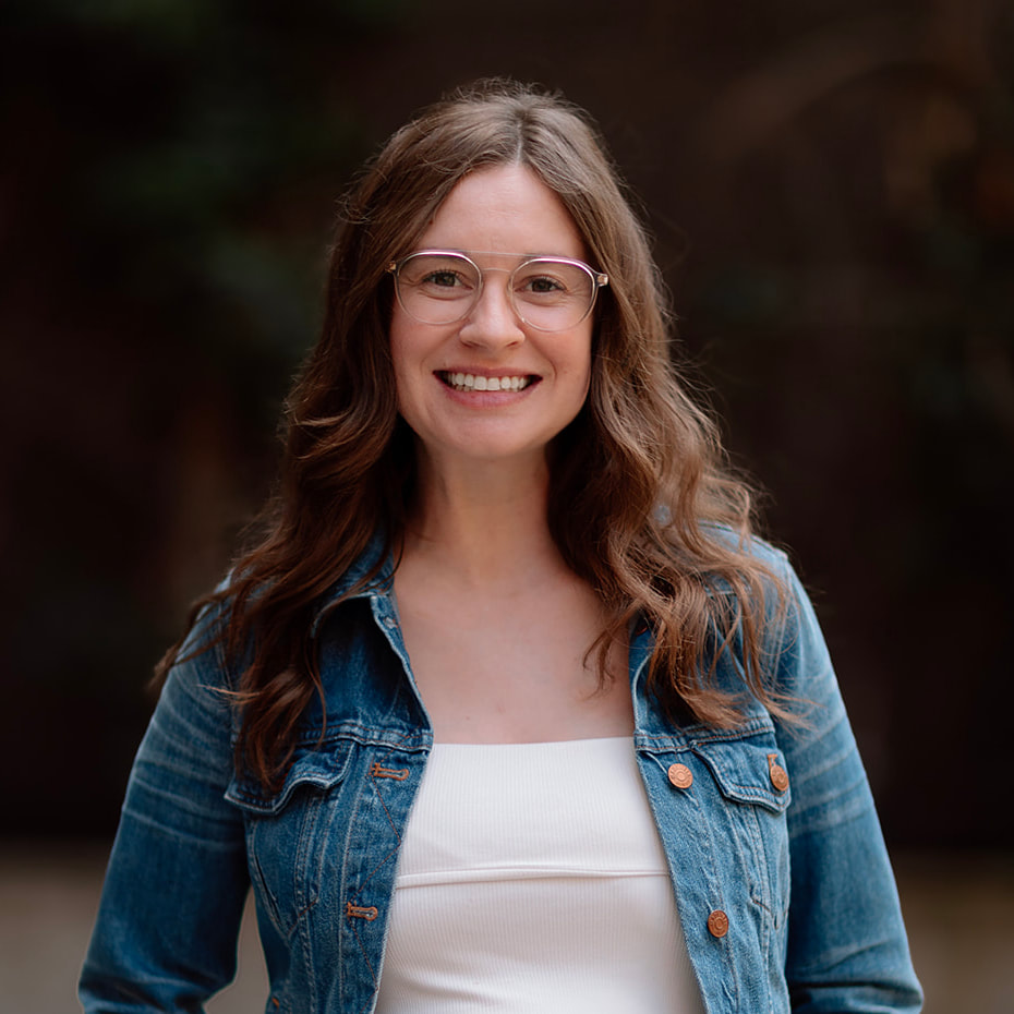 Our Team 8 Smiling woman with long brown hair, clear glasses, and a denim jacket.