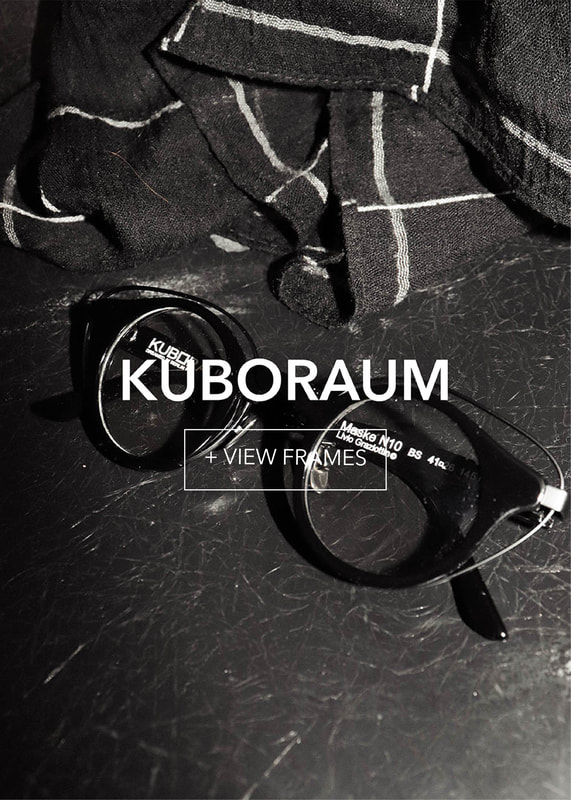 kuboraum-final1_3 Monochromatic image of black glasses on a dark, scratched surface, beside plaid fabric.