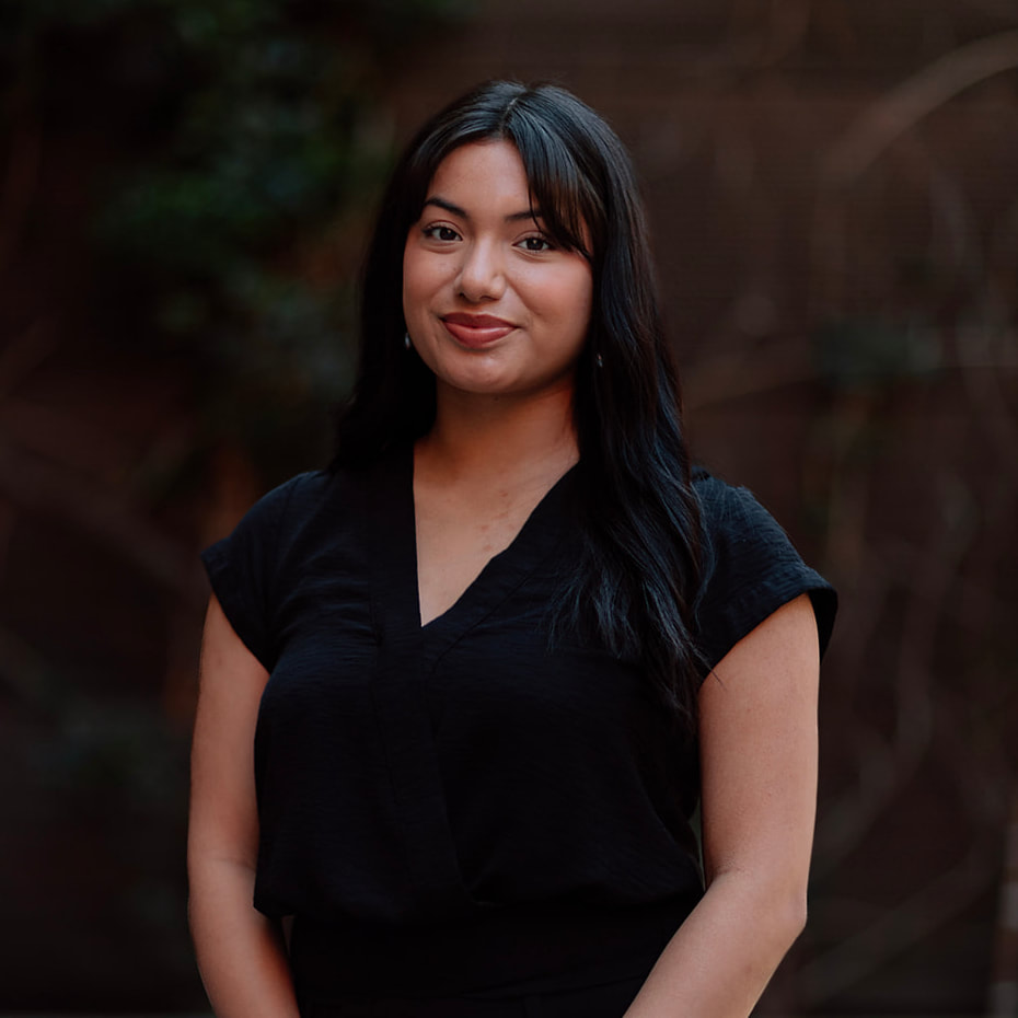 Our Team 13 Smiling young woman with dark hair and bangs, wearing a black v-neck top.