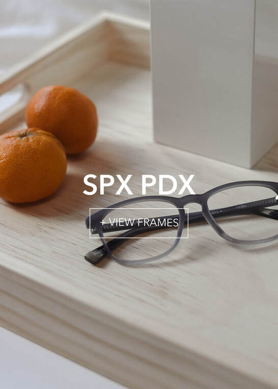 spdxpdx-final1_3 Stylish grey eyeglasses, two oranges, on a light wooden tray. SPX PDX and View Frames.