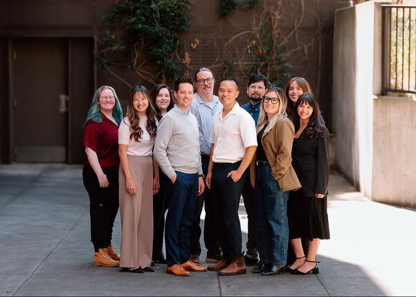 Diverse team of eleven professionals smiling happily outdoors on a sunny day.