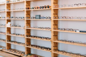 Numerous eyeglasses and sunglasses on light wooden shelves in a brightly lit optical store.