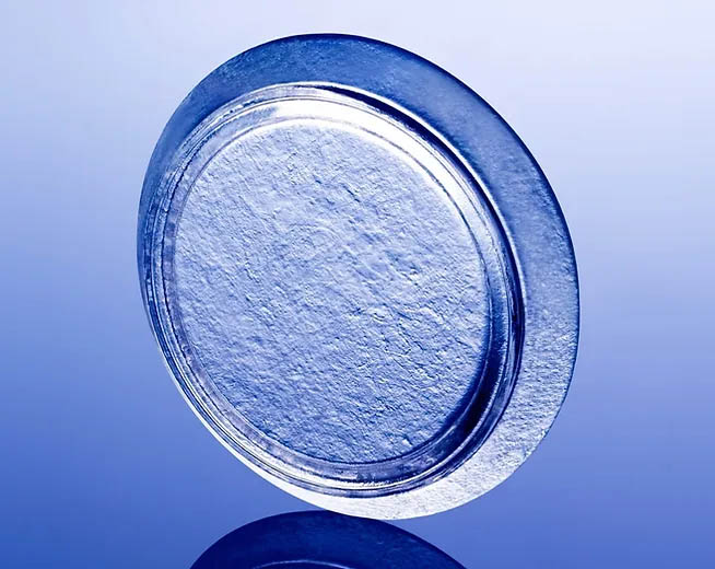 Textured metallic blue disc with a smooth outer ring, reflecting on a blue surface.