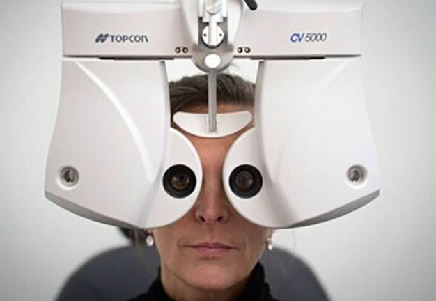 Home 11 Woman undergoing an eye exam, looking into a white Topcon CV 5000 refractor.