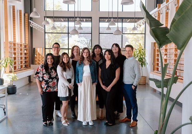Ten smiling colleagues pose in a bright, stylish eyewear boutique.