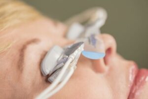Person's face with white medical sensors, wires, and blue pads attached near eyes and nose.